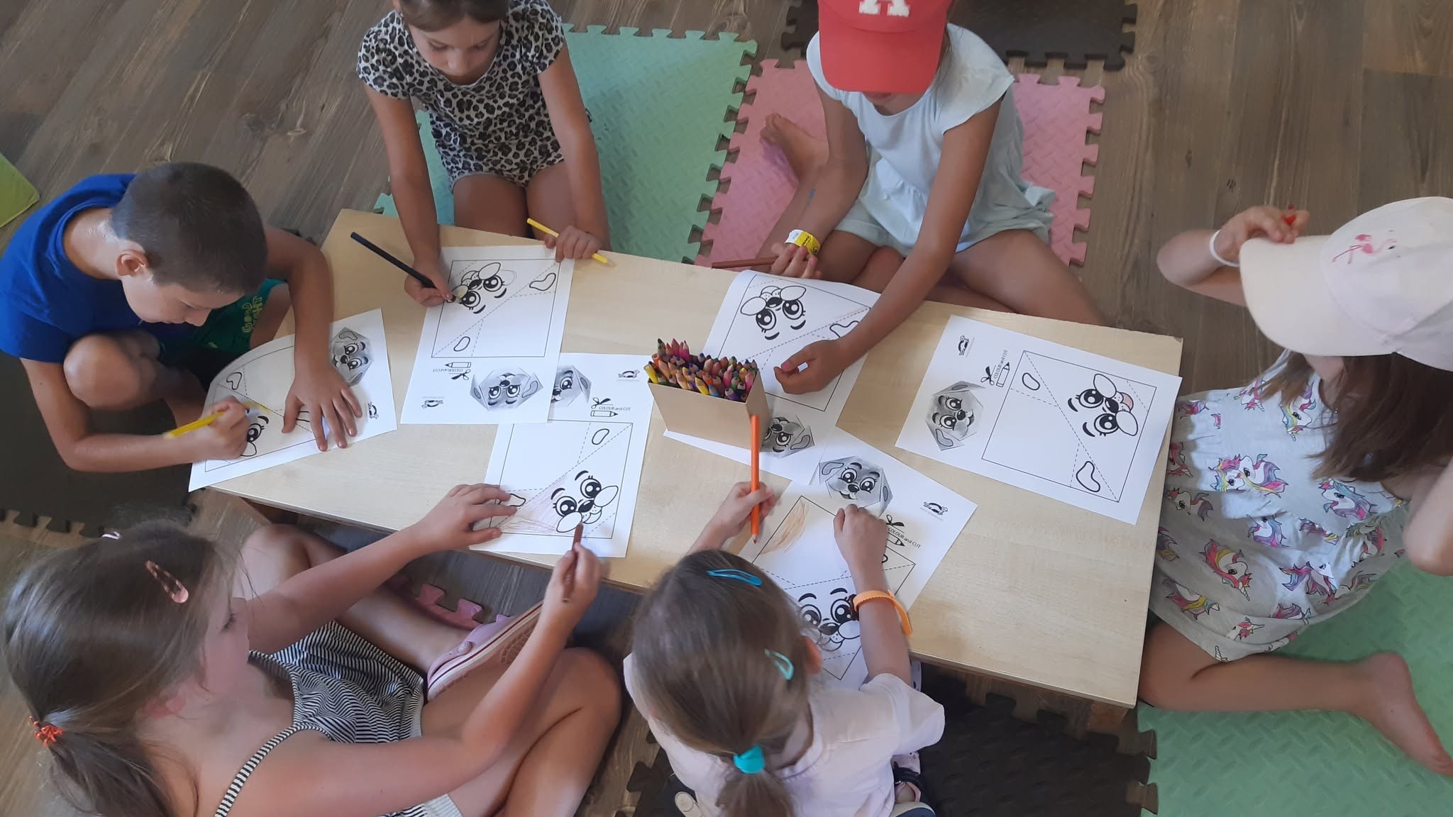 Gyerekek kutyás rajzokat színeznek egy alacsony asztal körül ülve