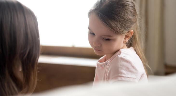 Kislány lehajtott fejjel ül a vele szemben ülő felnőttel beszélgetve